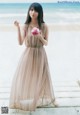 A woman in a long dress holding a cupcake on the beach.