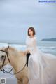 A woman in a white dress riding a horse on the beach.