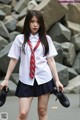 A woman in a school uniform is holding a pair of shoes.