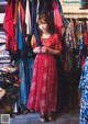 A woman in a red dress standing in front of a rack of clothes.