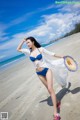 A woman in a blue bikini and a straw hat on the beach.