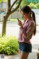 A woman standing next to a tree looking at her cell phone.