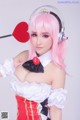 A woman with pink hair wearing headphones and holding a heart.