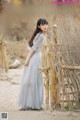 A woman in a long dress standing in front of a fence.