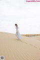 A woman in a blue dress standing on top of a sand dune.