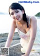 A woman in a white dress sitting on a rock by the water.