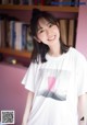 A woman standing in front of a bookshelf wearing a white shirt.