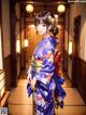 A woman in a blue kimono standing in a hallway.