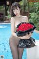 A woman holding a bunch of red roses by a pool.