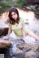 A woman in a yellow shirt is sitting in a stream.