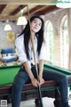 A woman sitting on top of a pool table holding a cue.