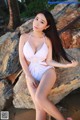 A woman in a white bathing suit sitting on a rock.